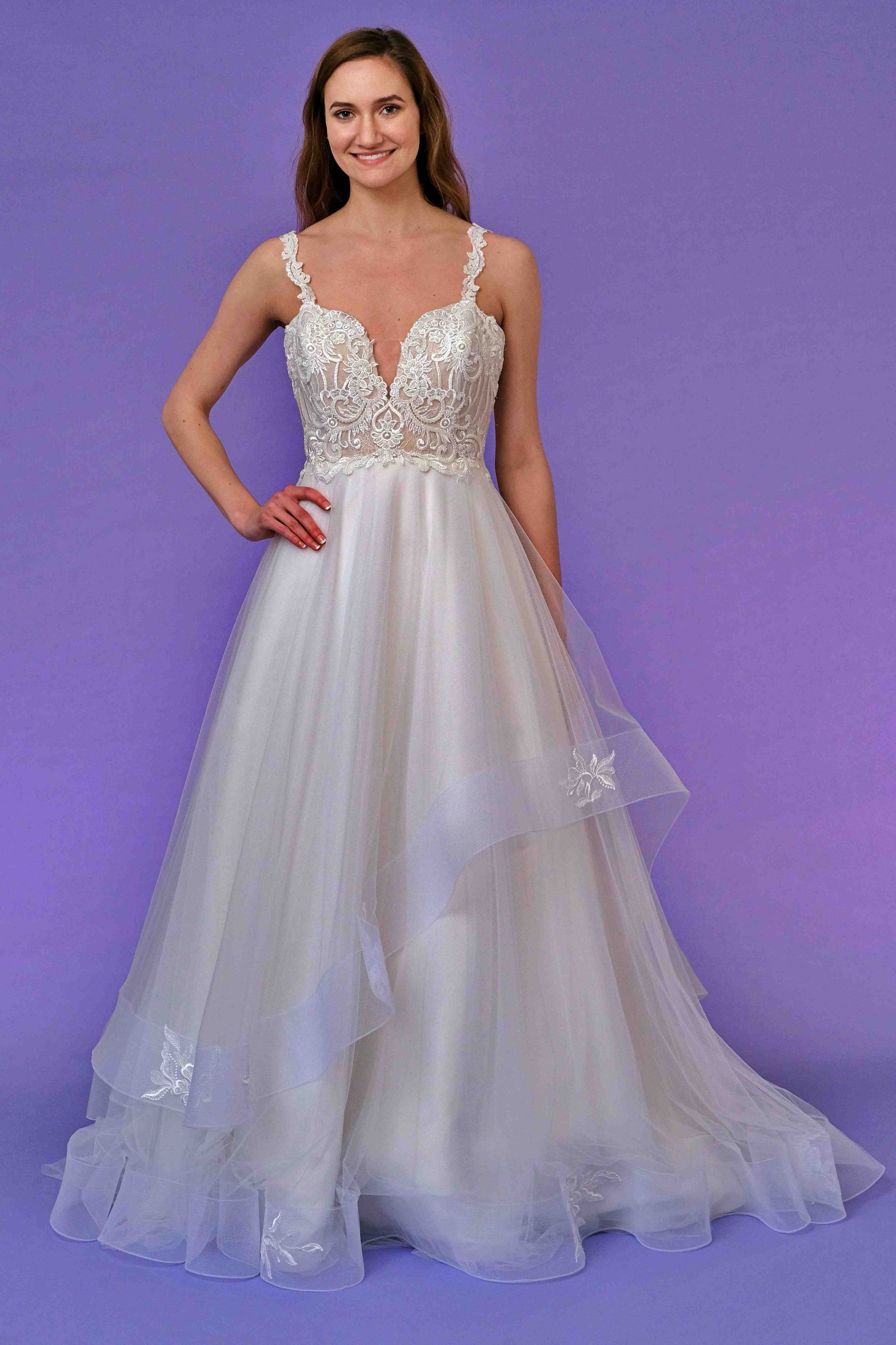 Woman in a white wedding dress with beading and tulle, posing on a purple background.