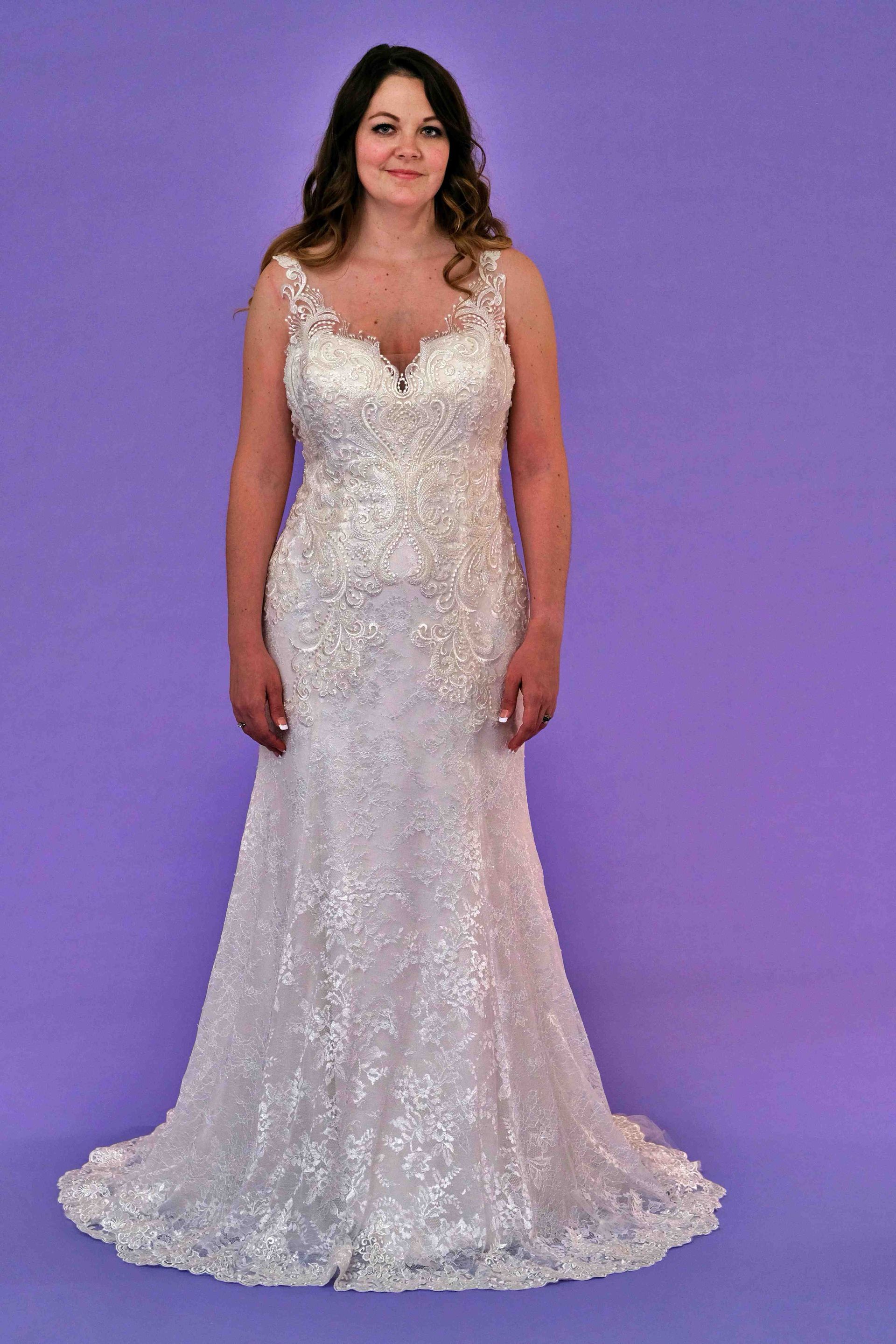 Woman in a white, sparkling wedding gown, standing against a purple backdrop.