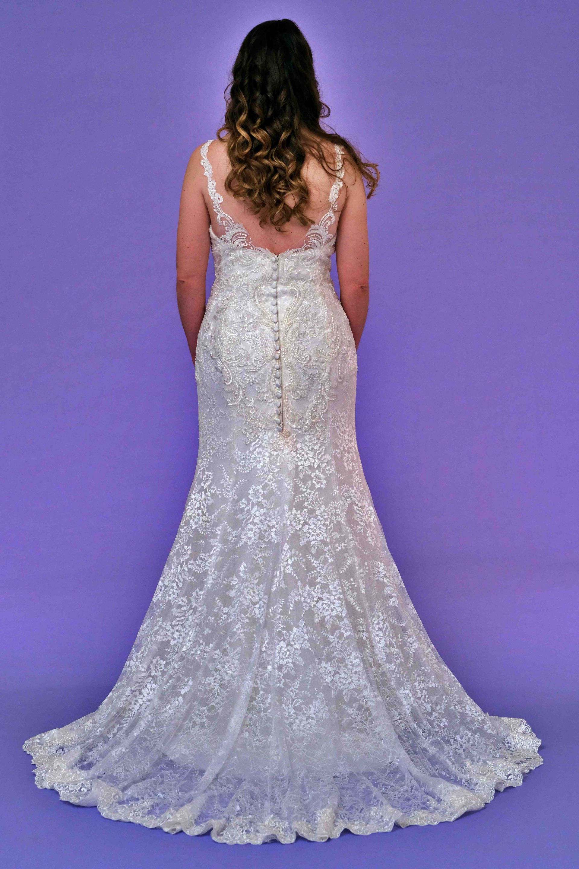 Woman in a white lace wedding dress, back view, on a purple background.