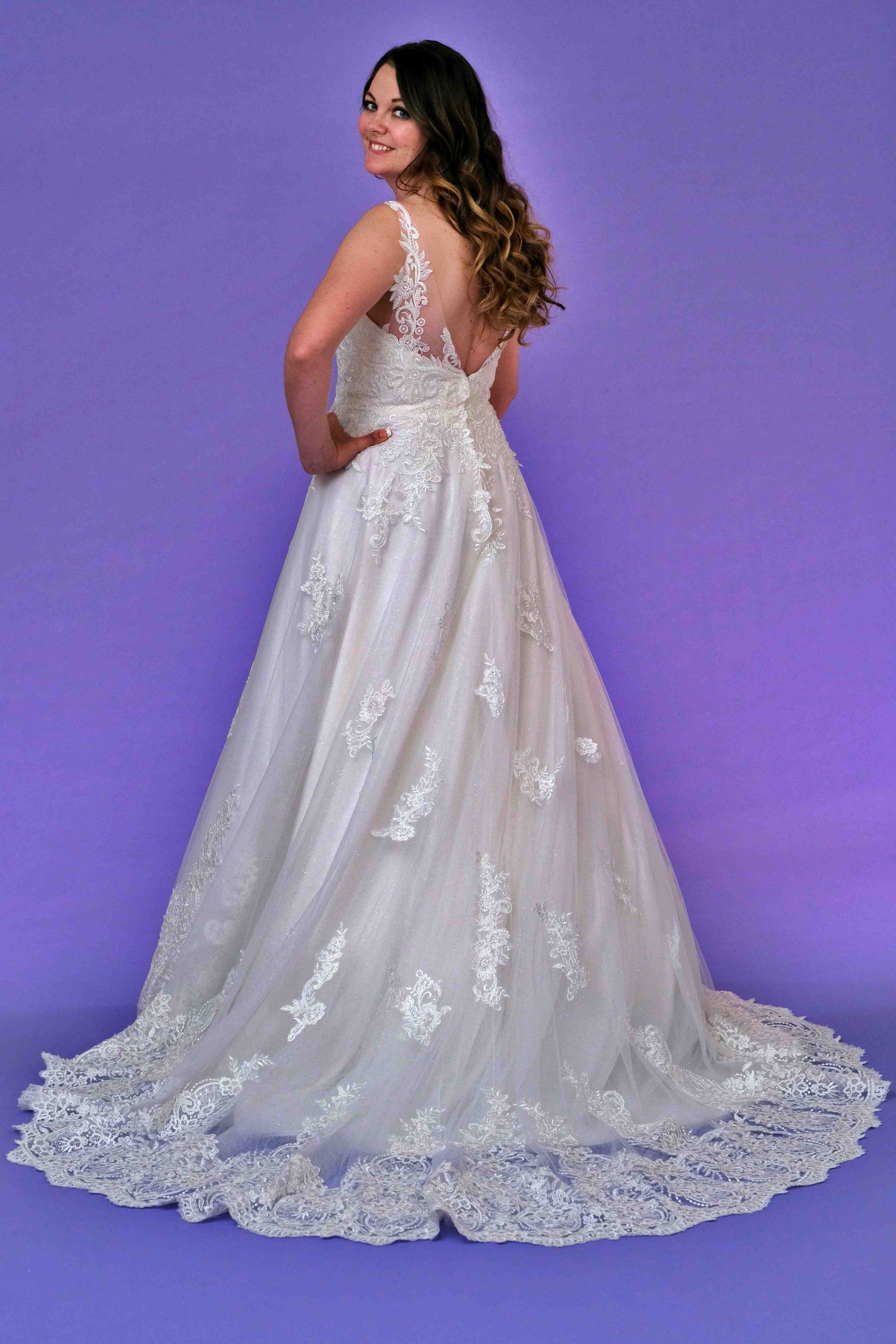 Woman in a white wedding gown, back turned, looking over her shoulder, on a purple backdrop.