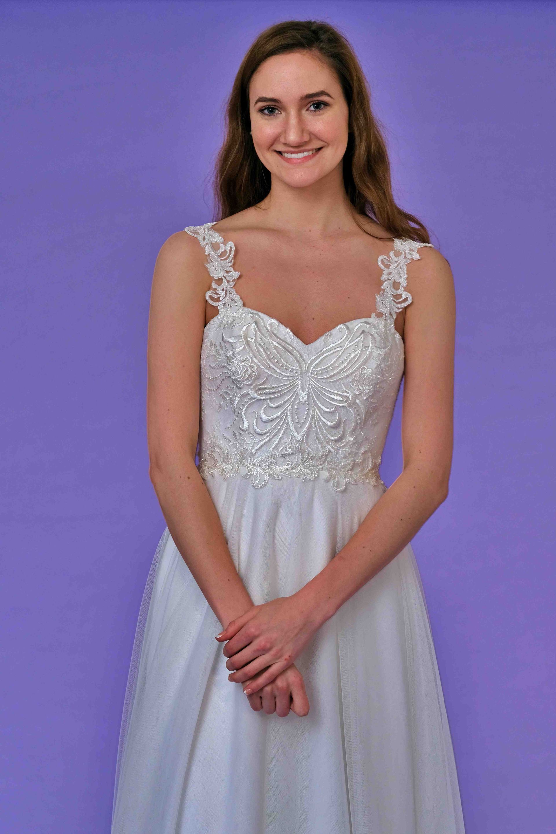 Woman in a white wedding dress with a decorated bodice smiles in front of a purple wall.