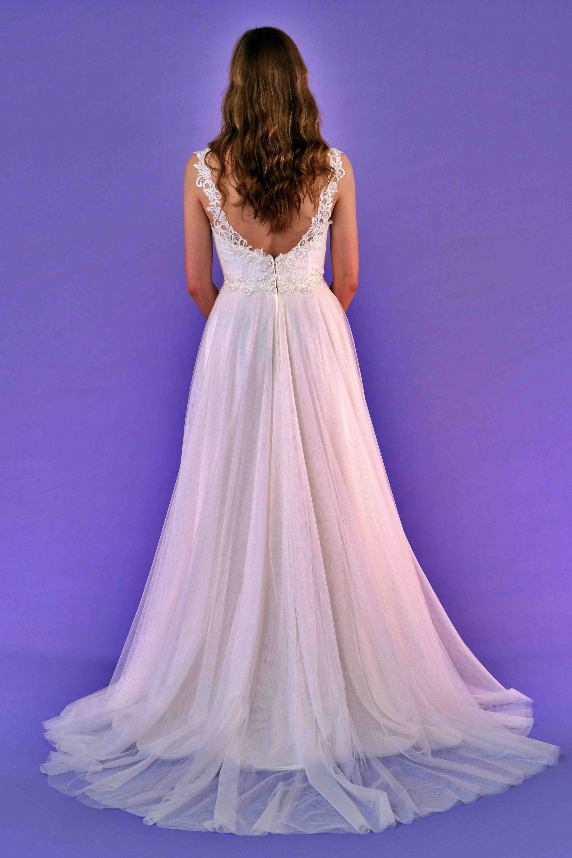 Woman in a white wedding dress, back view, standing against a purple background.