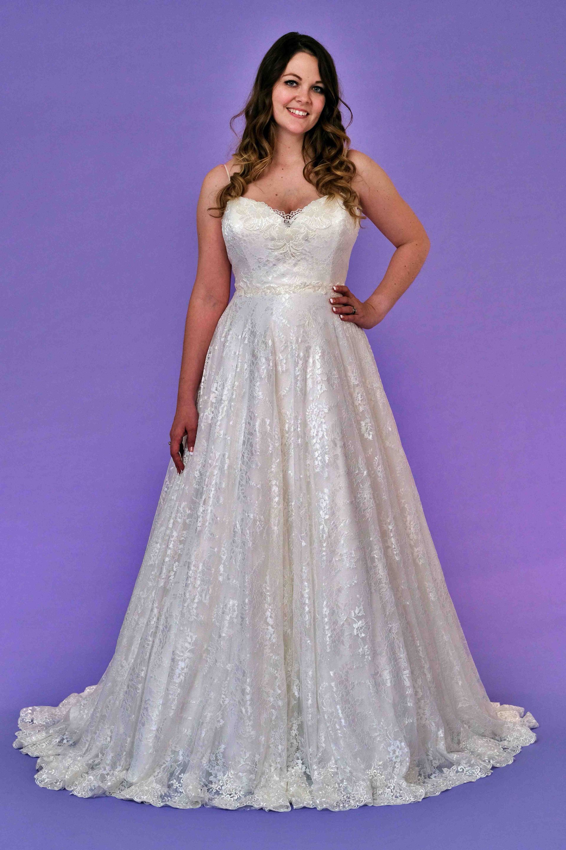 Woman in a white wedding dress with a sweetheart neckline, smiling on a purple background.