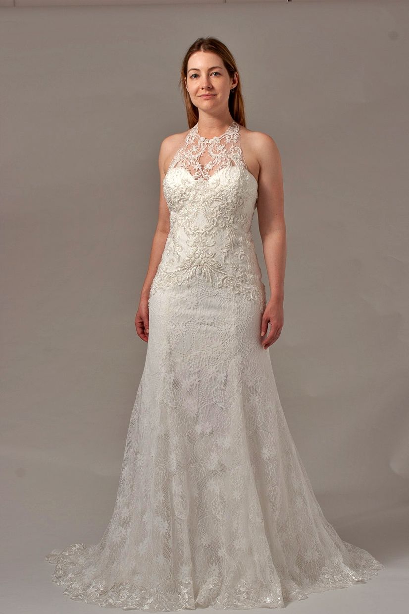 Woman in a white lace wedding dress with a high neckline, standing in a studio.