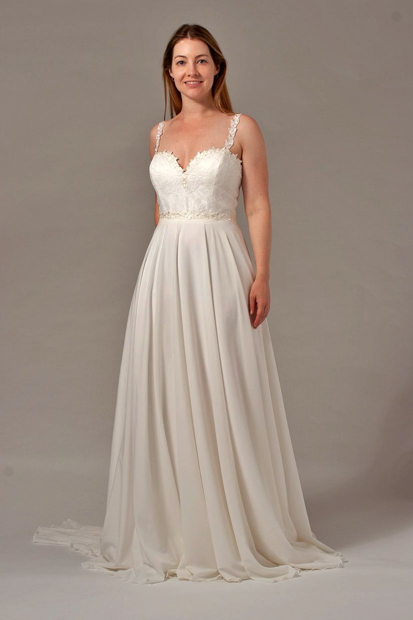 Woman in a white wedding dress, posing against a gray backdrop.