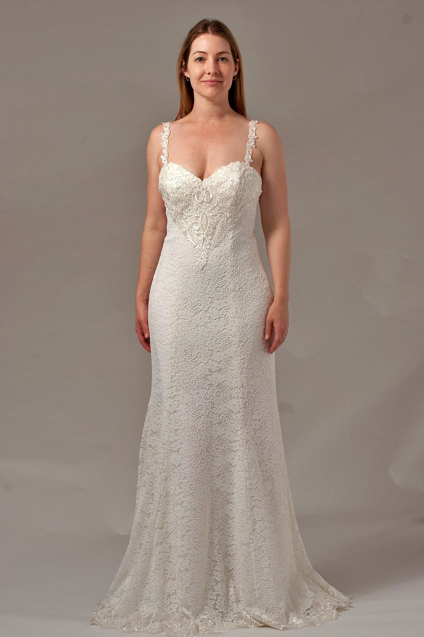 Woman in a white wedding gown with beaded bodice and spaghetti straps, posing in a studio.