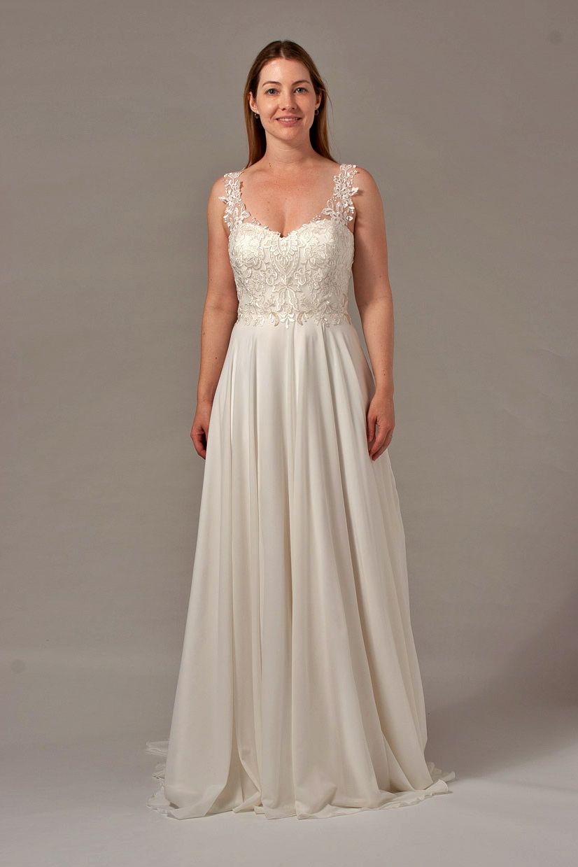 Woman wearing a white wedding dress with floral bodice, standing in a studio.