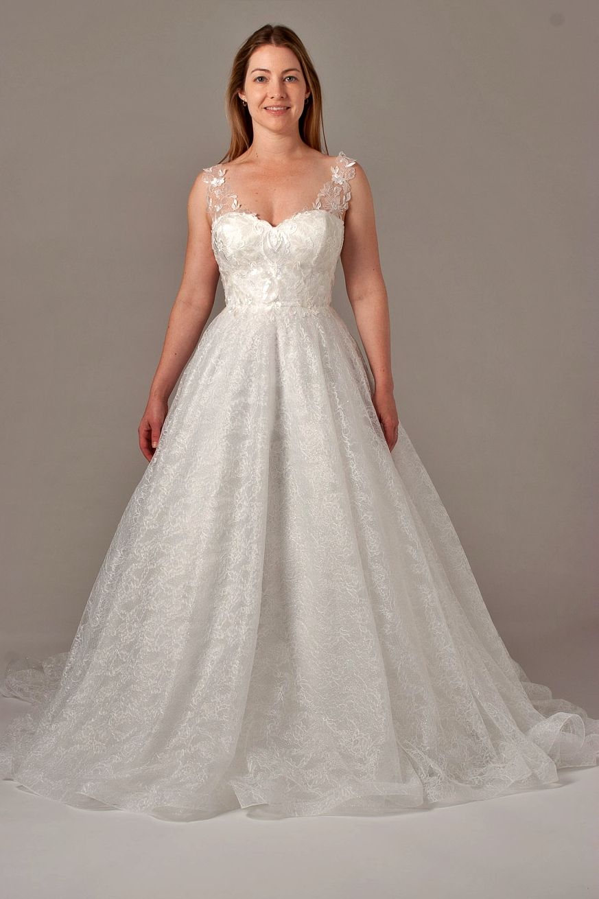 Woman in a white wedding gown smiles, standing against a neutral background.