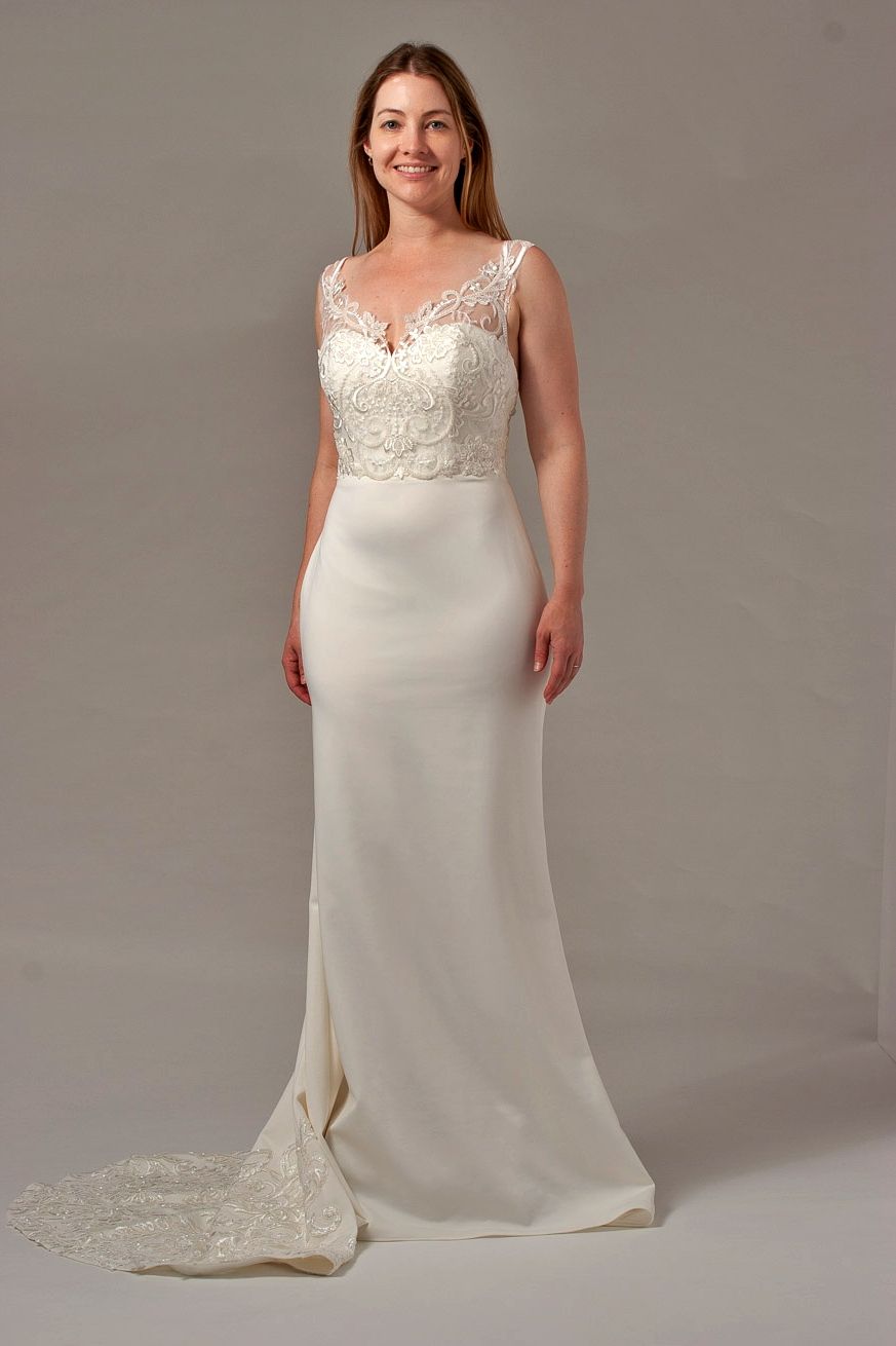 Woman in a white wedding dress with lace bodice, and a train, standing on a light gray background.