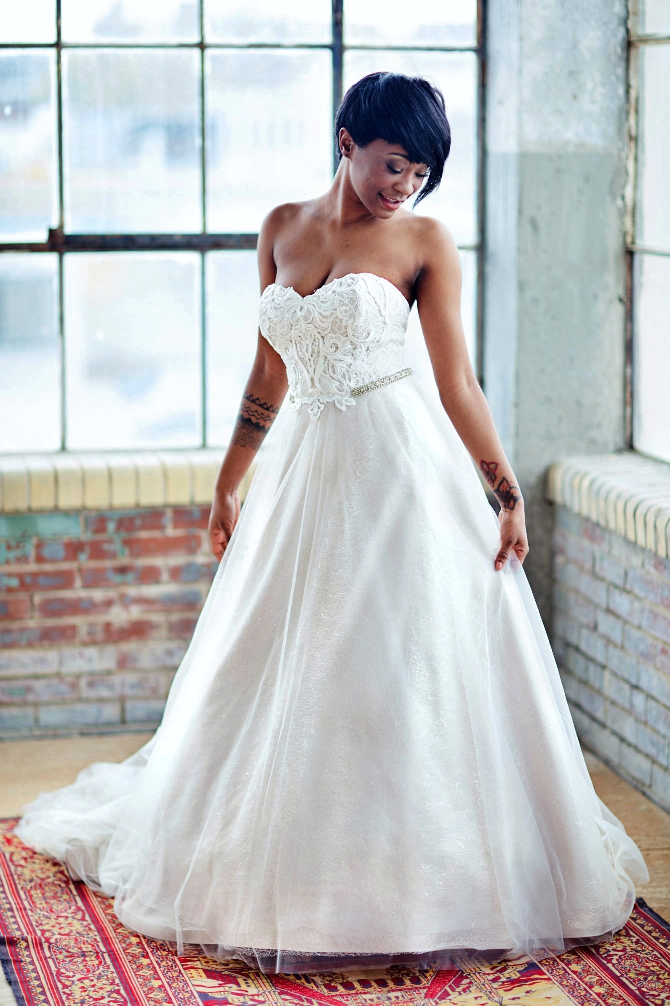 Woman in strapless wedding dress, smiling, near a window.