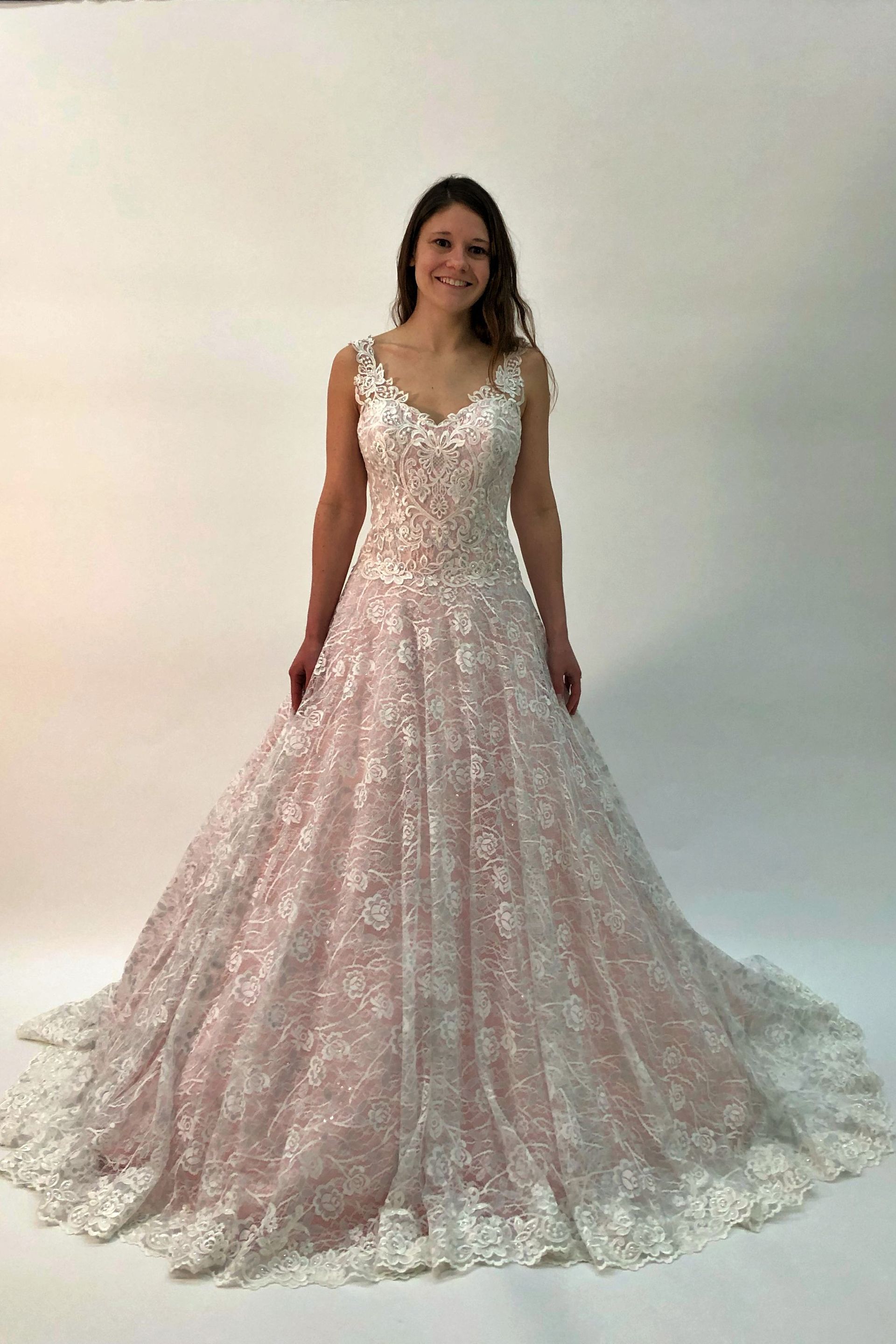 Woman in white lace wedding dress smiling in a studio.