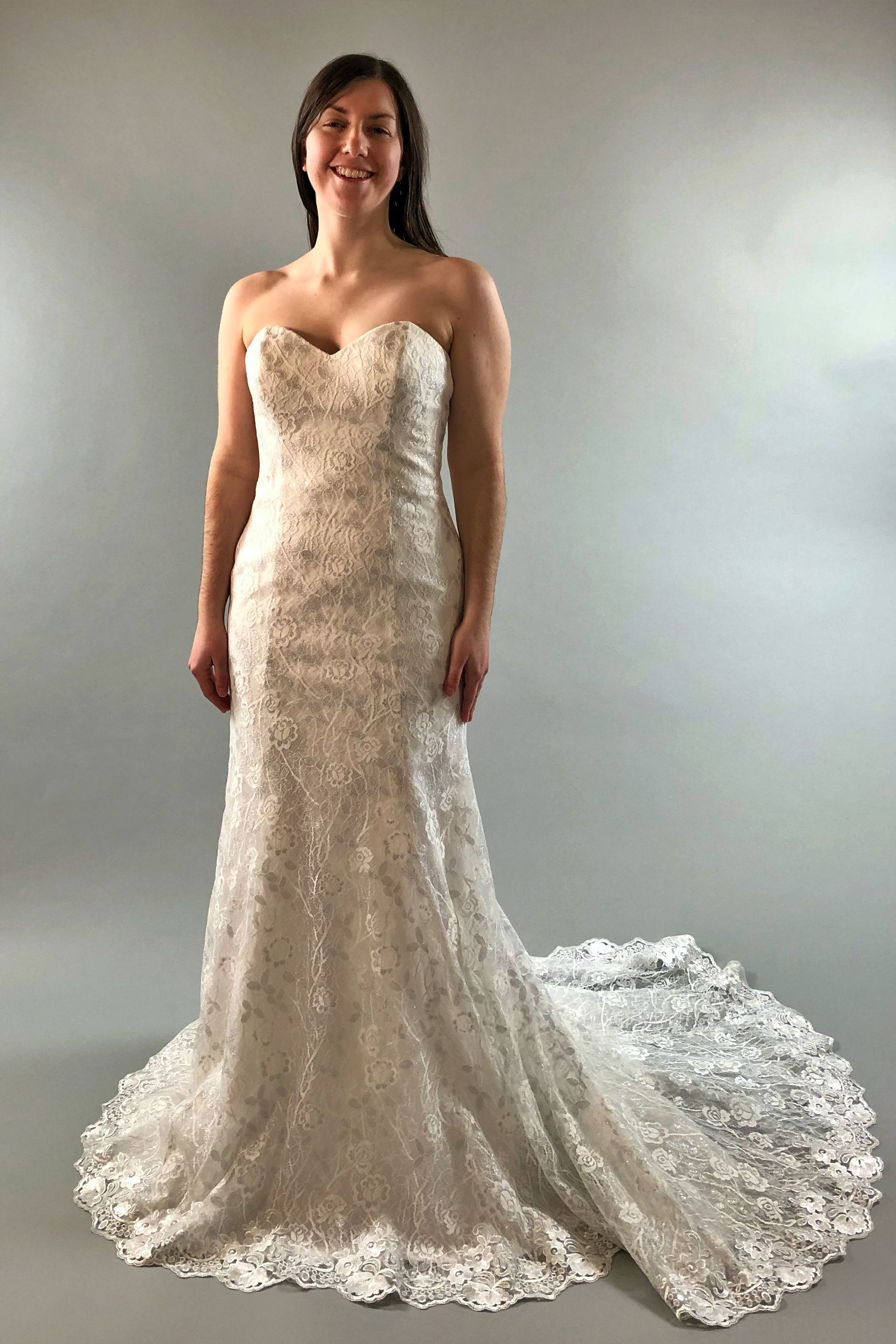 Woman in strapless wedding dress with long train, smiling in a studio setting.