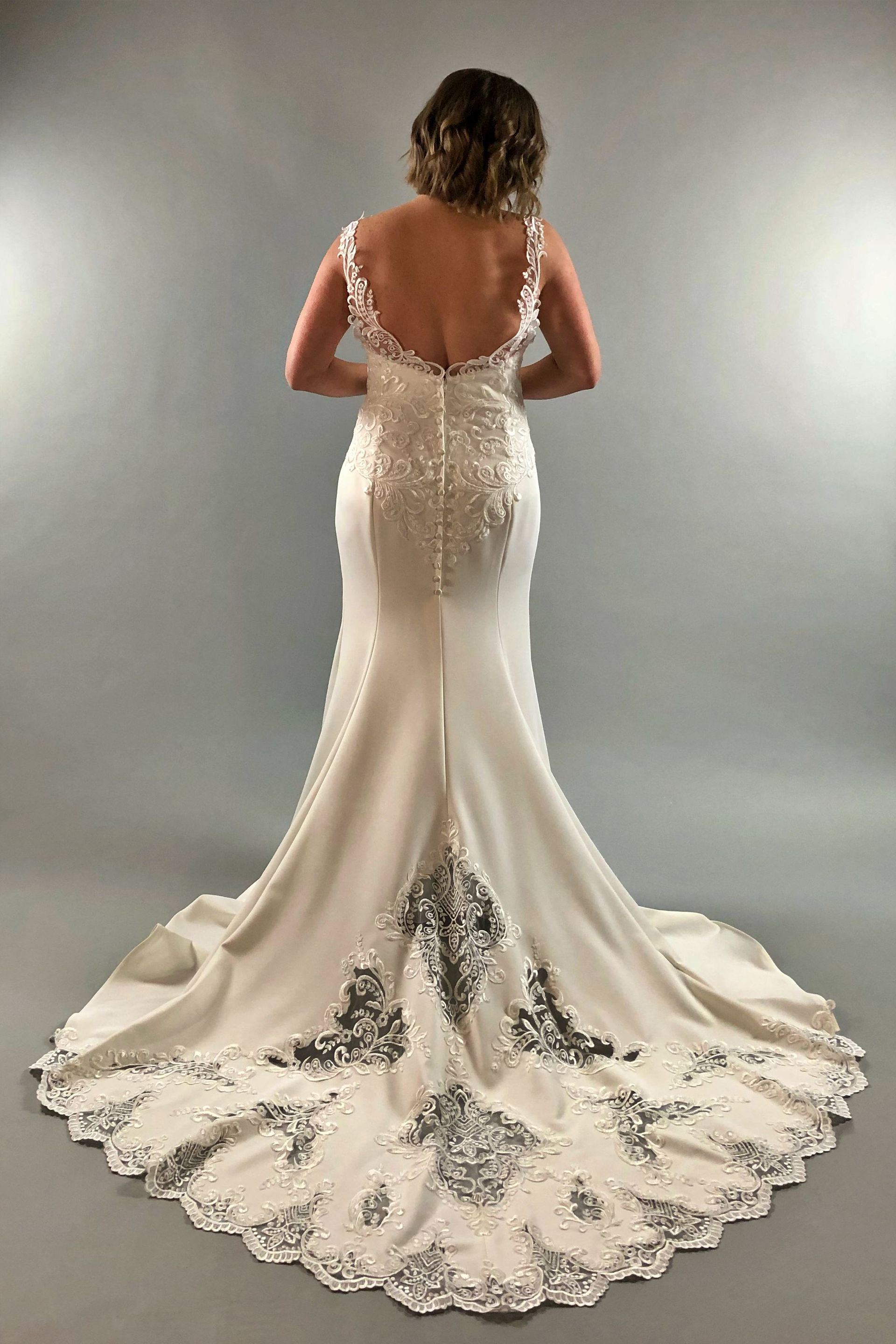 Woman in a white wedding dress, back view, with low back, detailed skirt and train on a gray background.