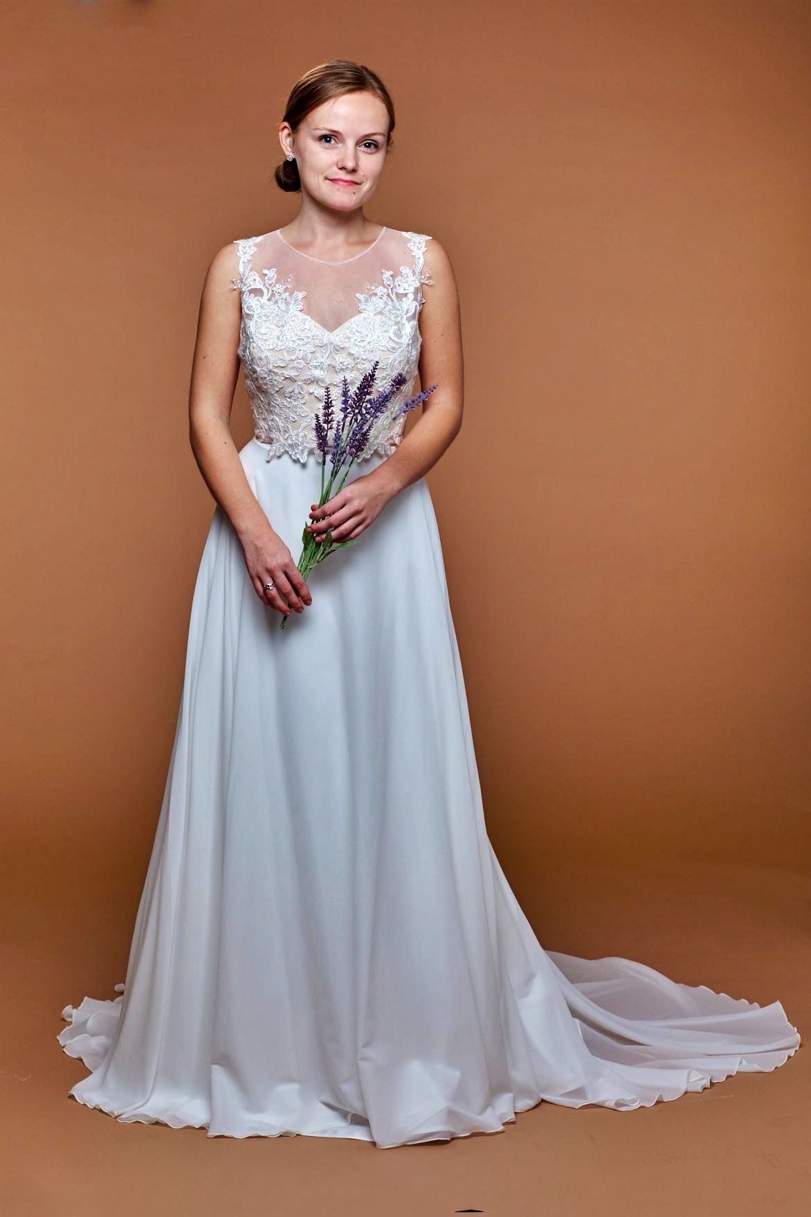 Woman in a white wedding dress holds lavender against a brown backdrop.