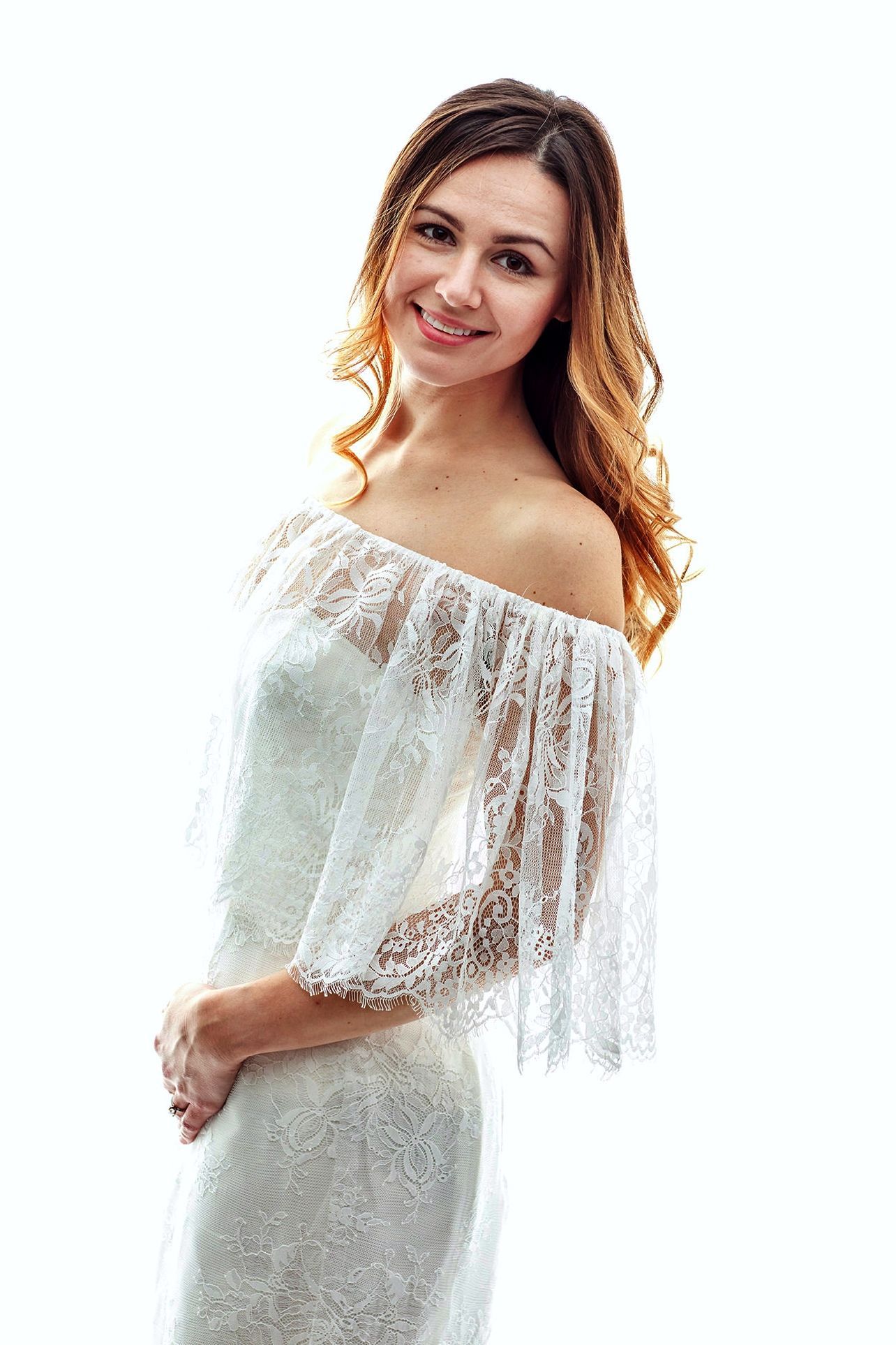 Woman in a white lace off-the-shoulder dress smiling.