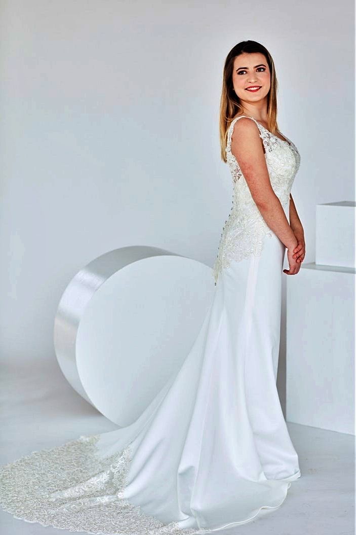 Woman in a white wedding dress with a long train, posing in a studio with white props.