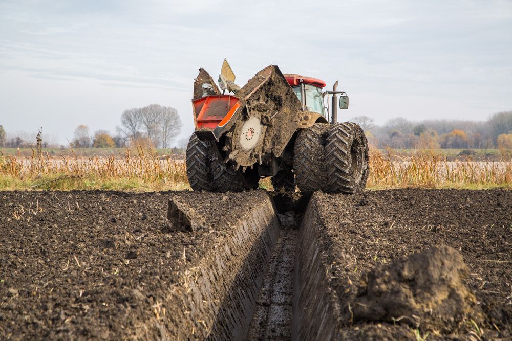 Tractor With Large Tires Digging a Trench in a Muddy Field — Rhino Excavator & Bobcat Hire in Trinity Beach, QLD