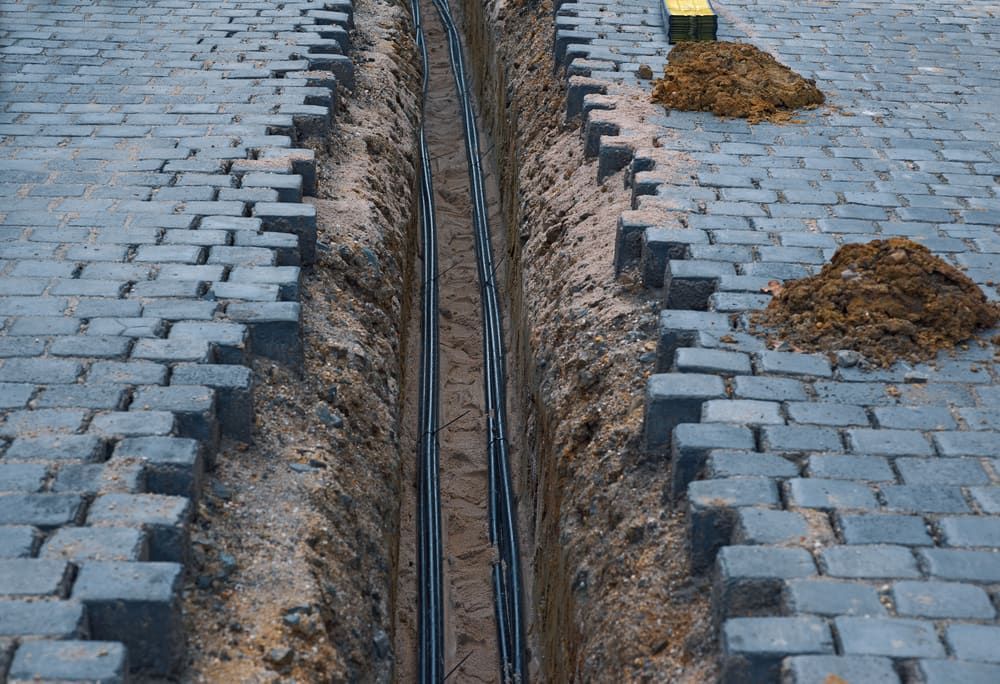 Trench Dug in a Cobblestone Path, Containing Dark Cables — Rhino Excavator & Bobcat Hire in Trinity Beach, QLD