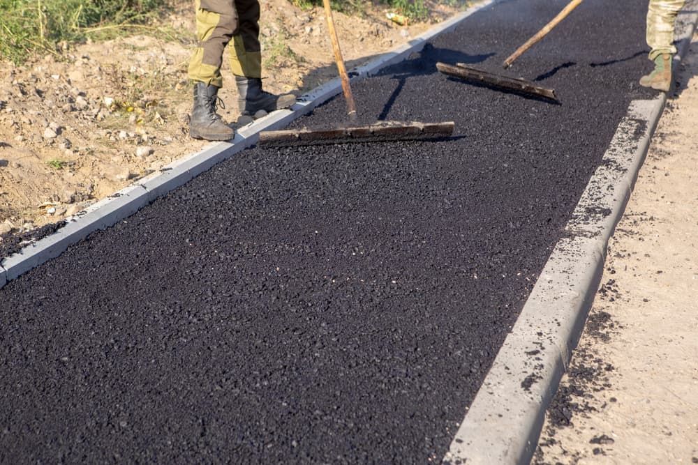 Road Workers Leveling Fresh Asphalt With Rakes on a Newly Paved Sidewalk — Rhino Excavator & Bobcat Hire in Gordonvale, QLD 