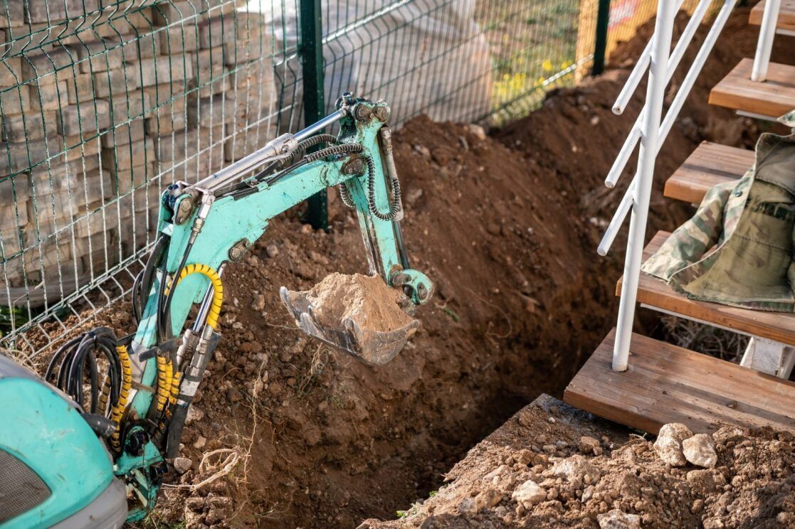 A Small Excavator Digs a Trench Near a Fence and Stairs — Rhino Excavator & Bobcat Hire in Trinity Beach, QLD