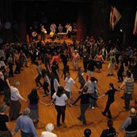 A large group of people are dancing in a circle on a wooden floor.