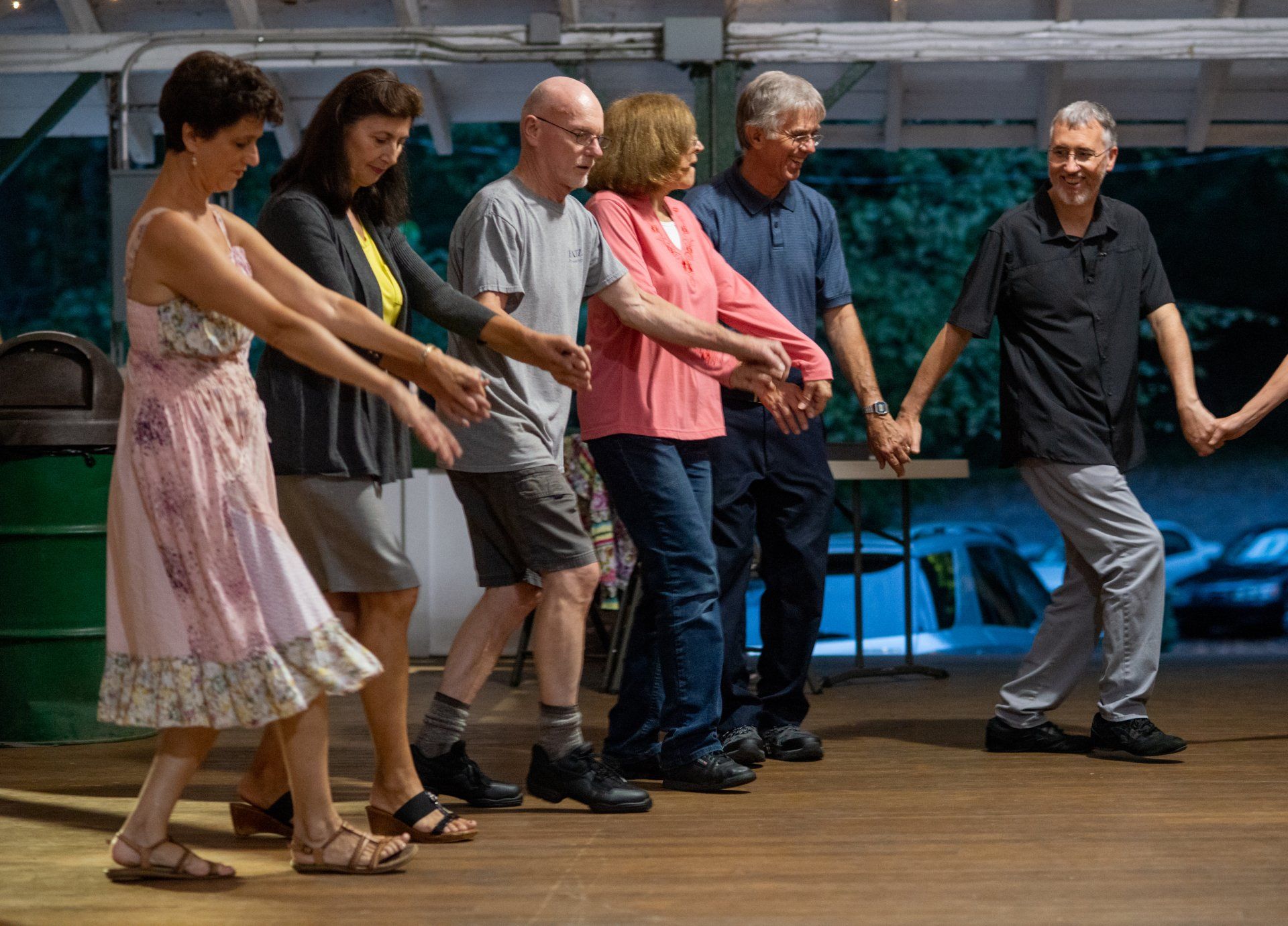 A group of people are holding hands and dancing on a wooden floor.