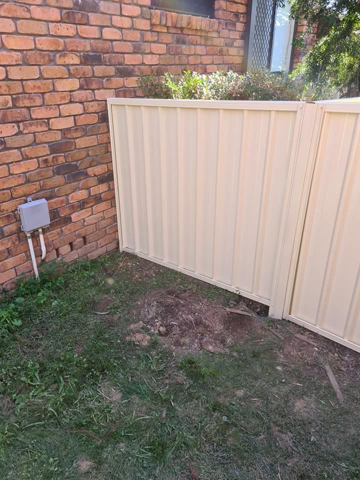 A White Fence Is Sitting in Front of A Brick Wall — D & B Fencing in Nabiac, NSW
