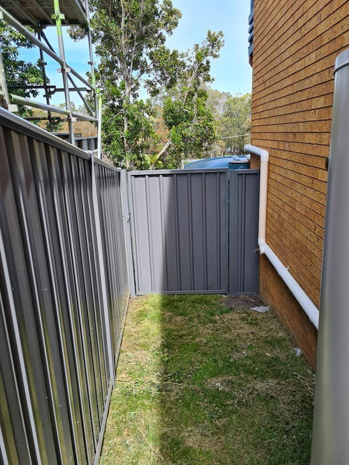 A Fence Is Surrounding a Grassy Area Next to A Brick Building — D & B Fencing in Taree, NSW