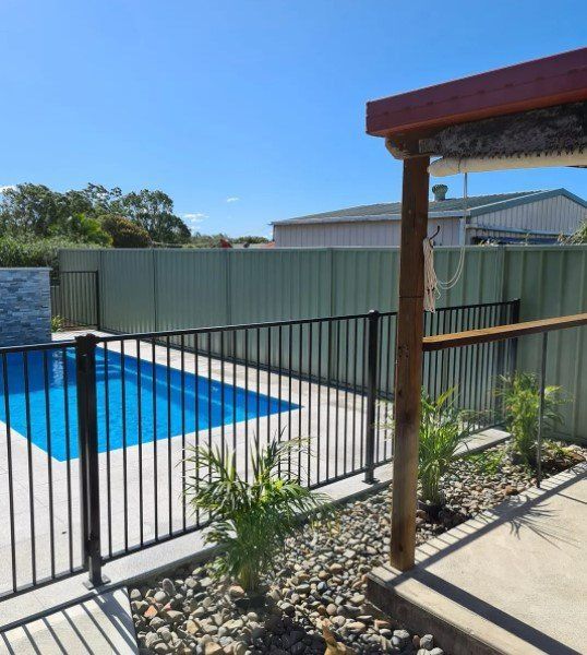A Fence Surrounds a Swimming Pool in A Backyard — D & B Fencing in Harrington, NSW