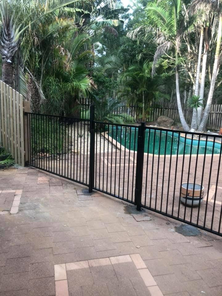 A Black Metal Fence Surrounds a Swimming Pool in A Backyard — D & B Fencing in Taree, NSW