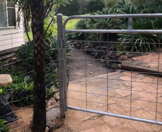 A Fence with Barbed Wire Surrounding a Brick Walkway Leading to A House — D & B Fencing in Taree, NSW