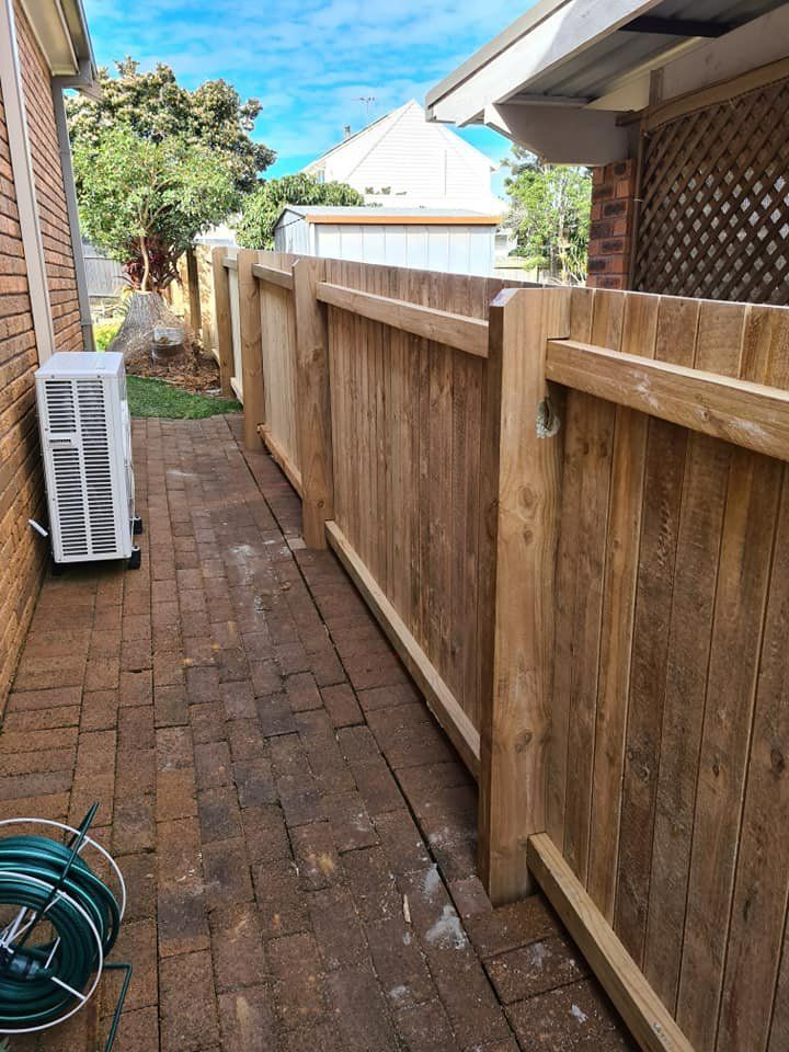 A Wooden Fence Surrounds a Brick Walkway Next to A House — D & B Fencing in Taree, NSW