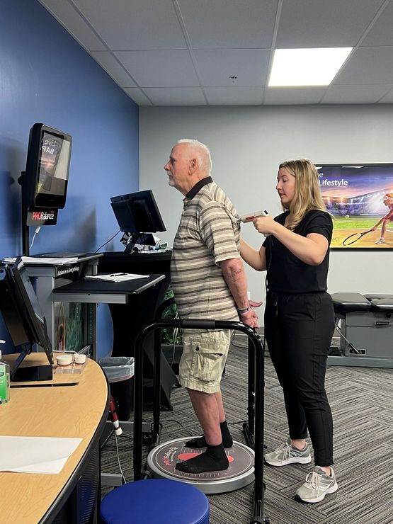 Woman assists man using a standing workstation in an office.