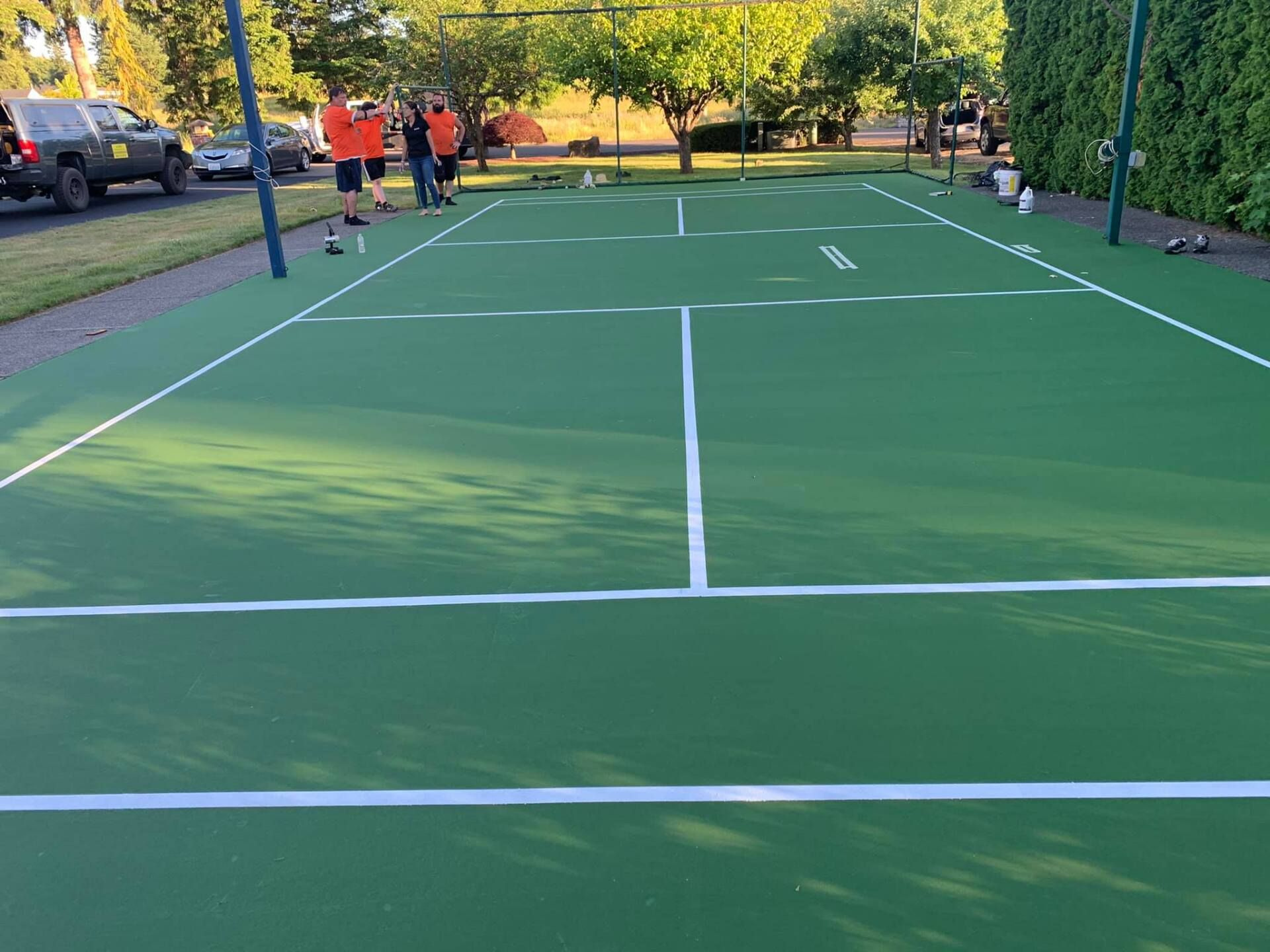 A group of people are standing on a green tennis court.