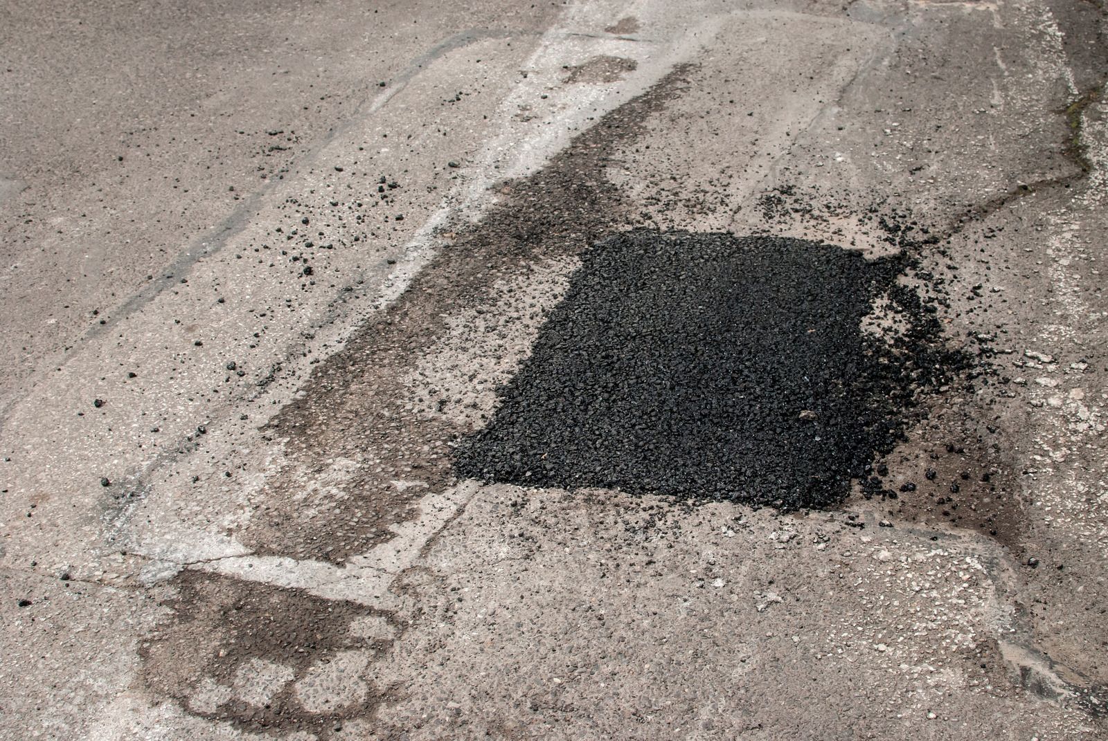 A yellow truck is laying asphalt on the side of a road.