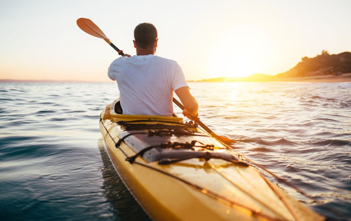 A man is paddling a yellow kayak in the ocean at sunset.