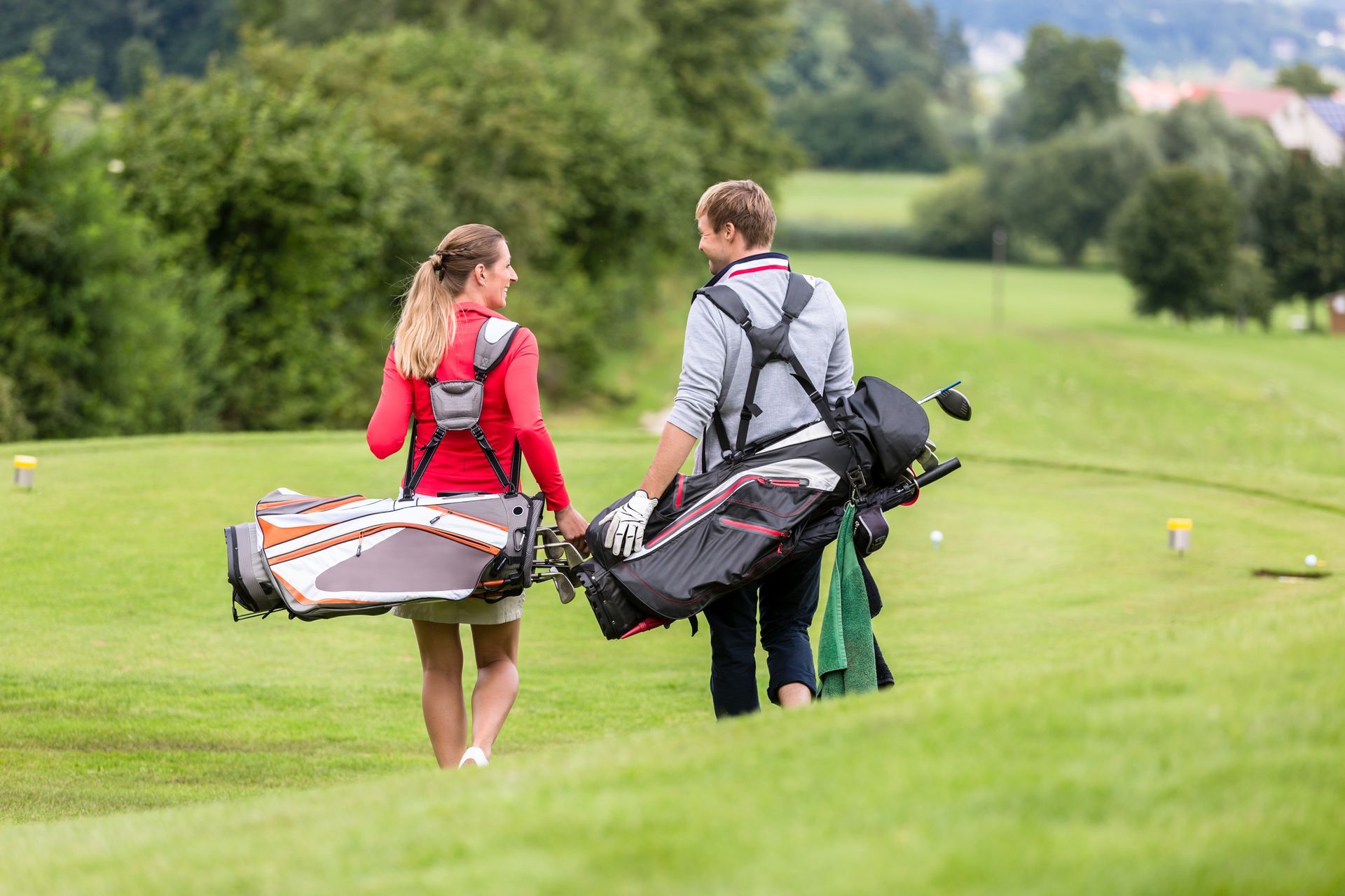 A man and a woman are walking down a golf course carrying golf bags.