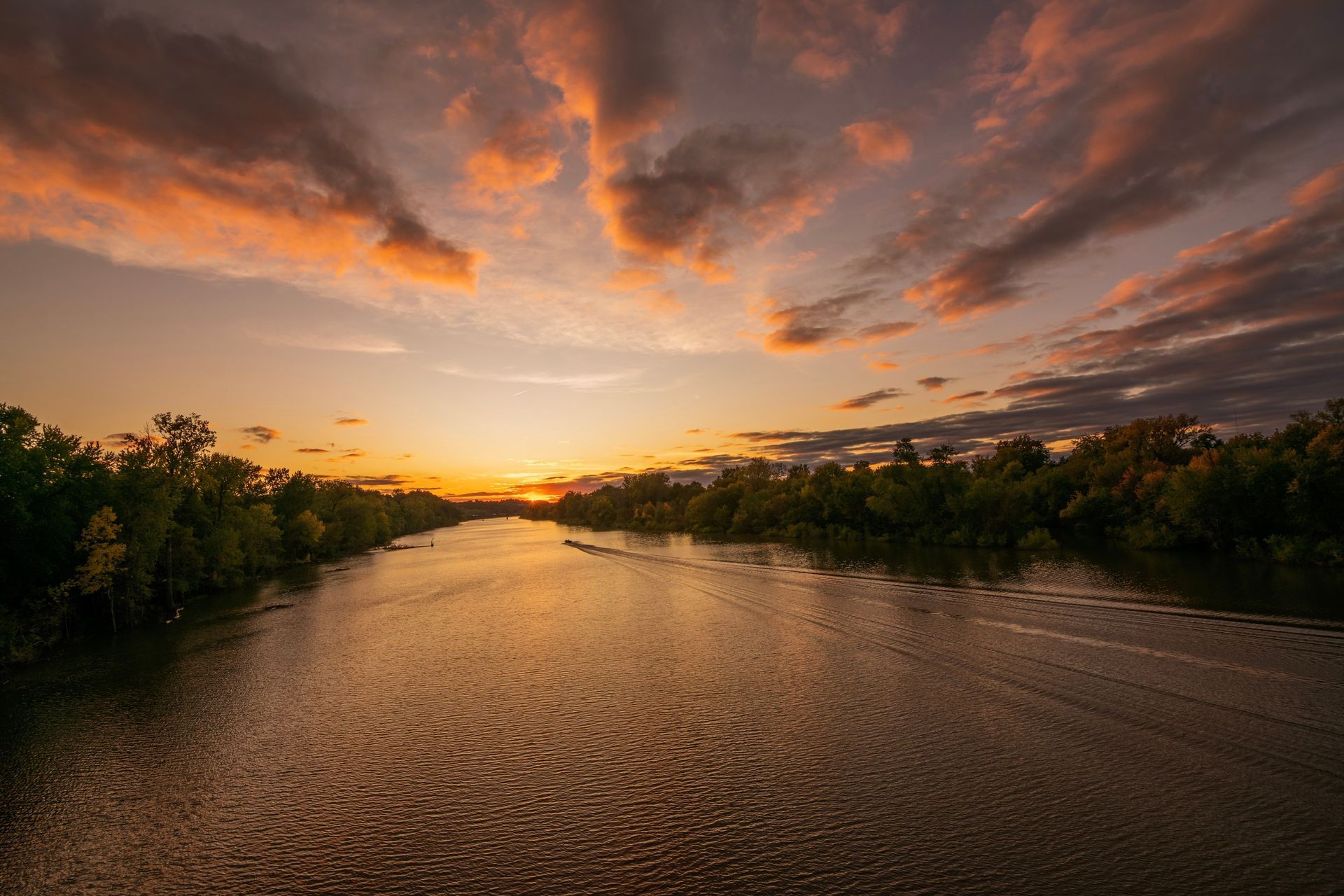 The sun is setting over a river surrounded by trees.