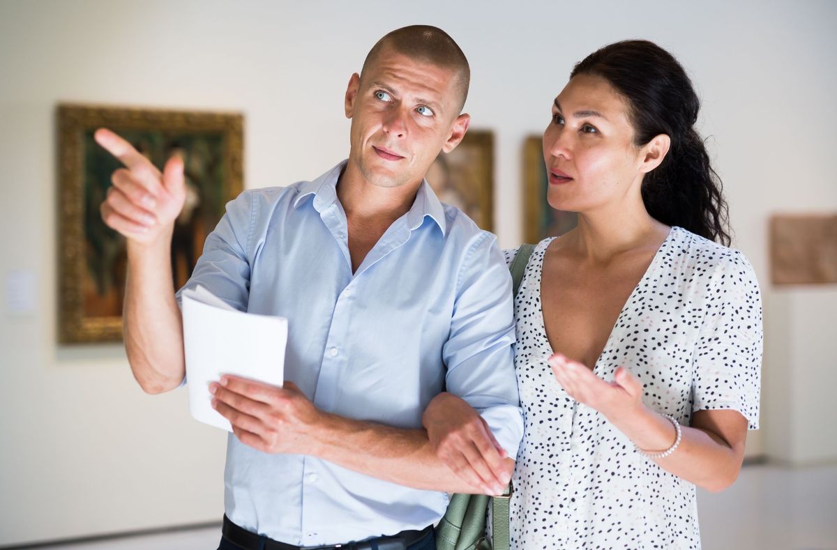 A man and a woman are looking at a painting in a museum.
