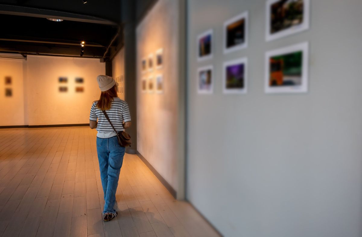 A woman is walking through a museum looking at paintings on the walls.