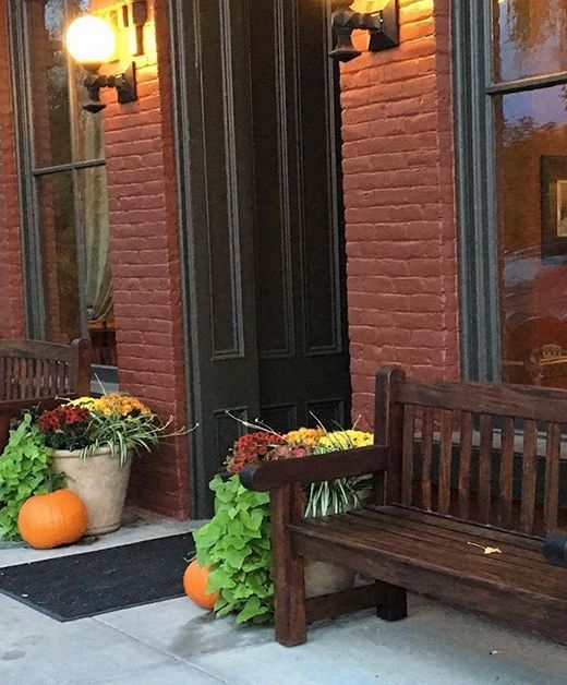 A wooden bench with pumpkins and flowers on it in front of a brick building