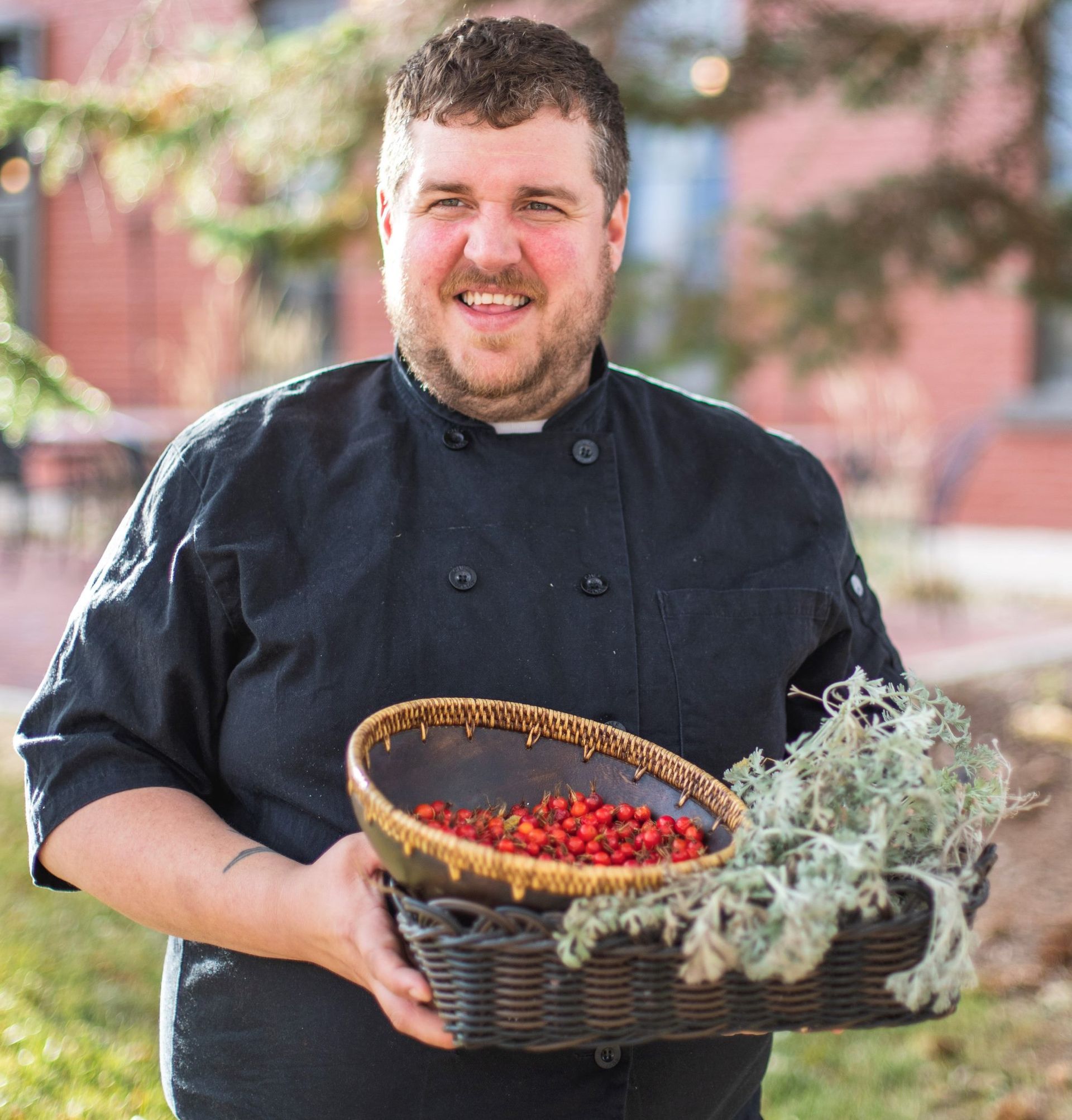 A man in a chef 's uniform is holding a basket of berries.