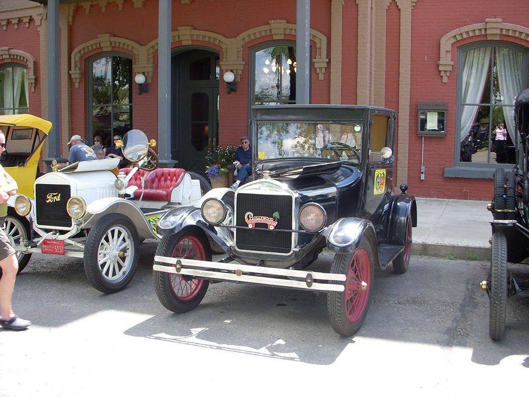 Three old cars are parked in front of a red building.