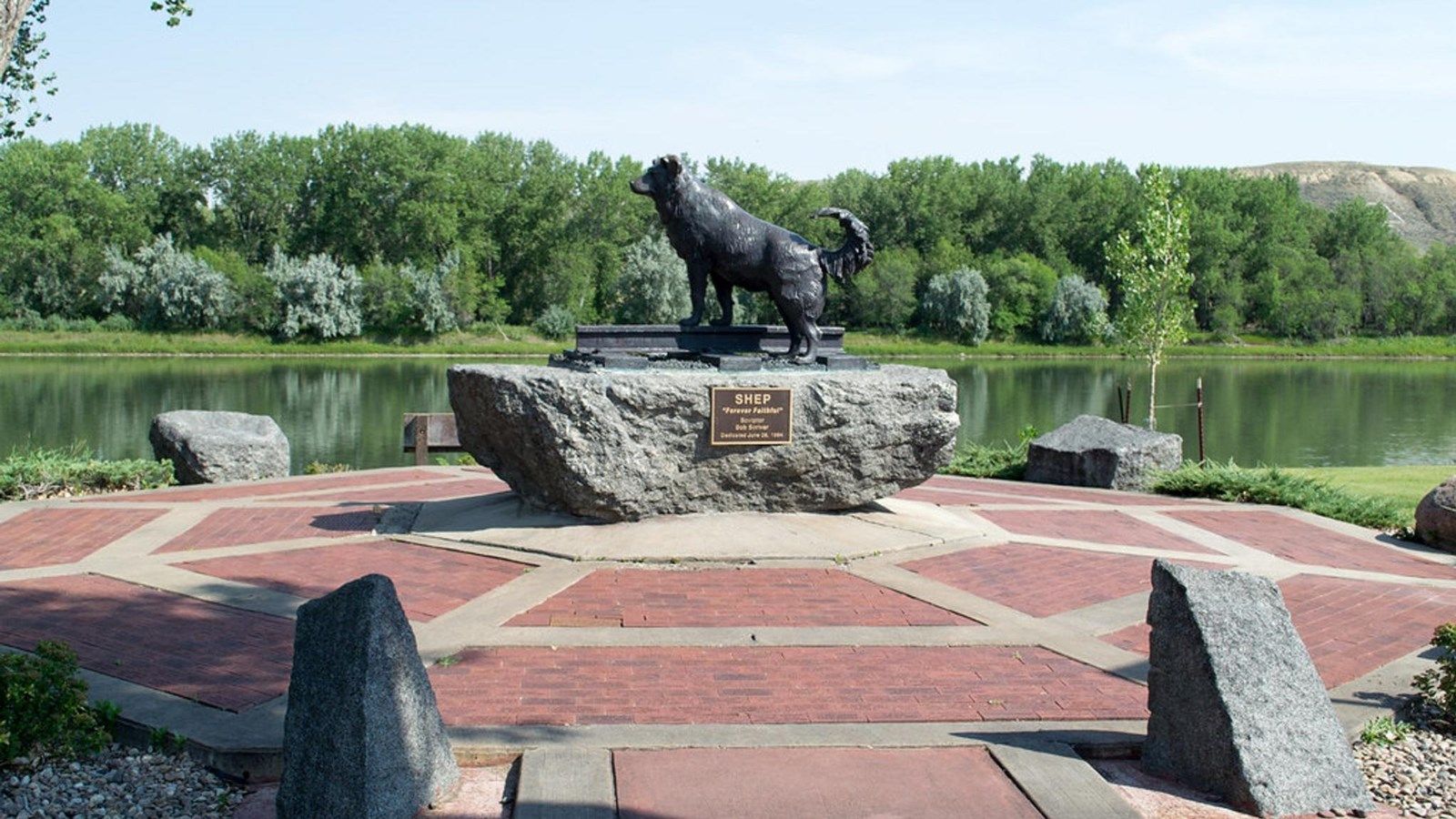 A statue of a dog standing on a rock in front of a lake