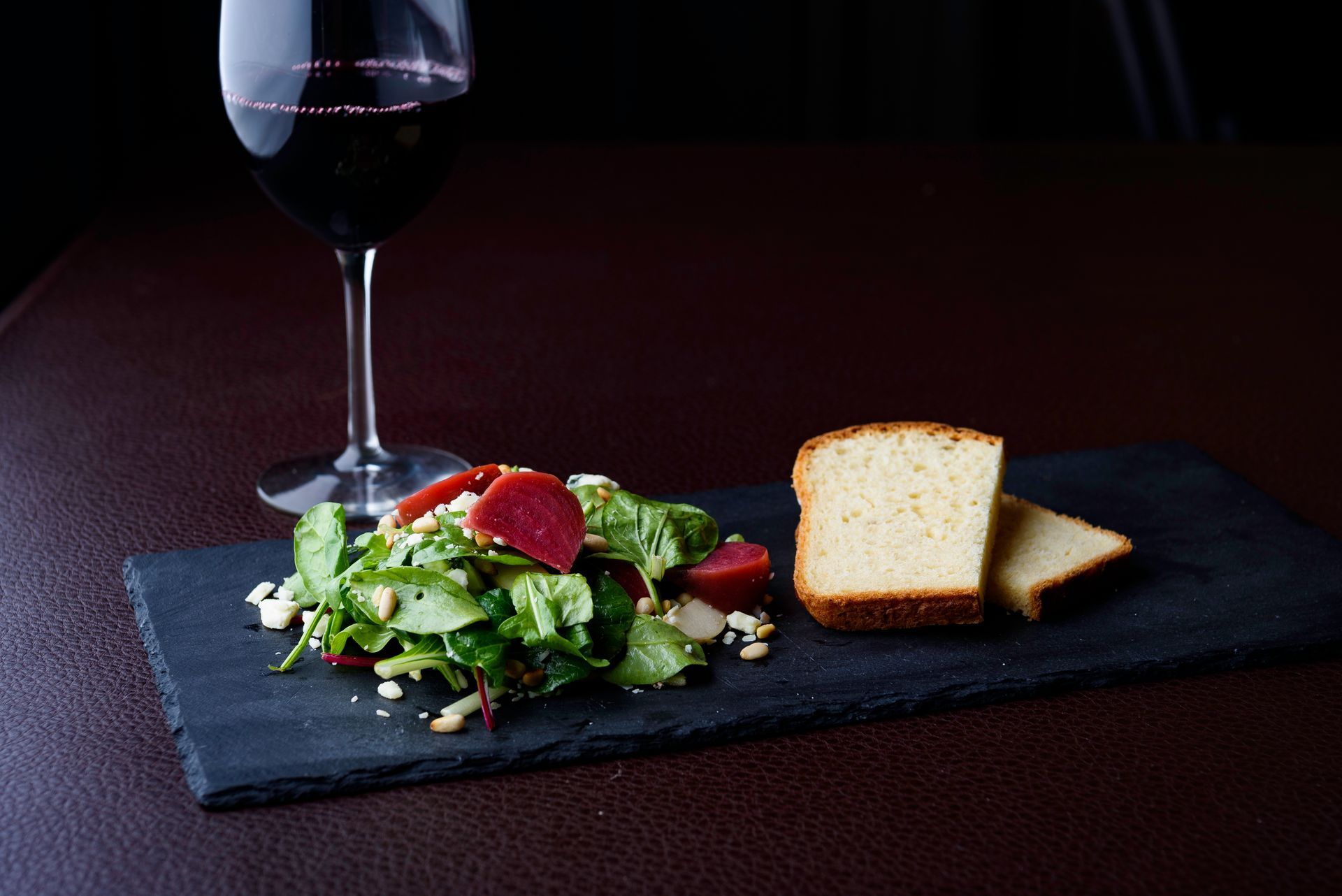 A salad and bread are on a cutting board next to a glass of wine.