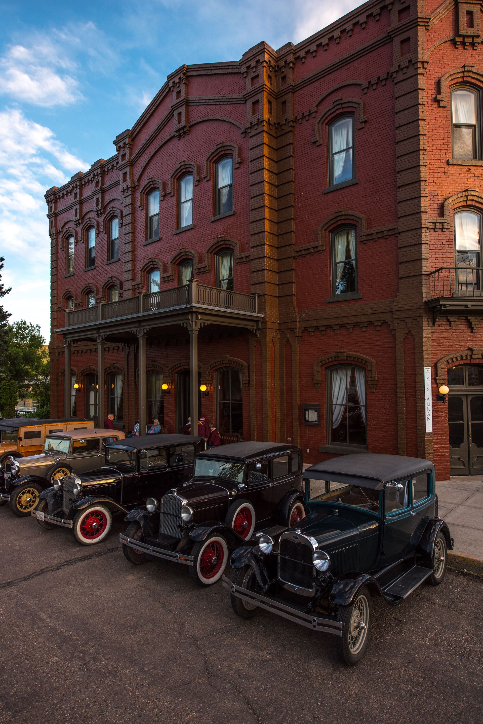 Three old cars are parked in front of a brick building.