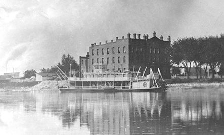 A black and white photo of a boat in the water with a building in the background.