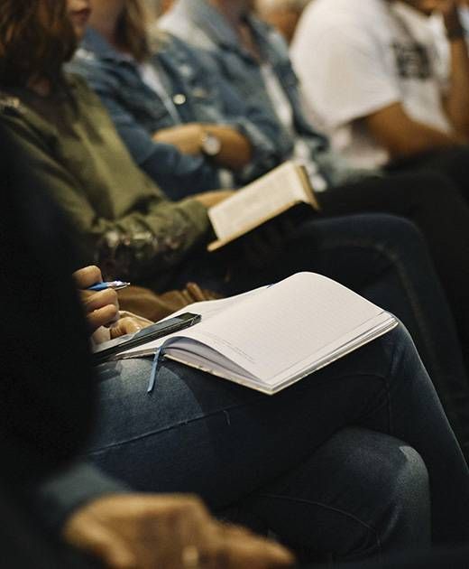 A group of people are sitting in a row holding books and notebooks.