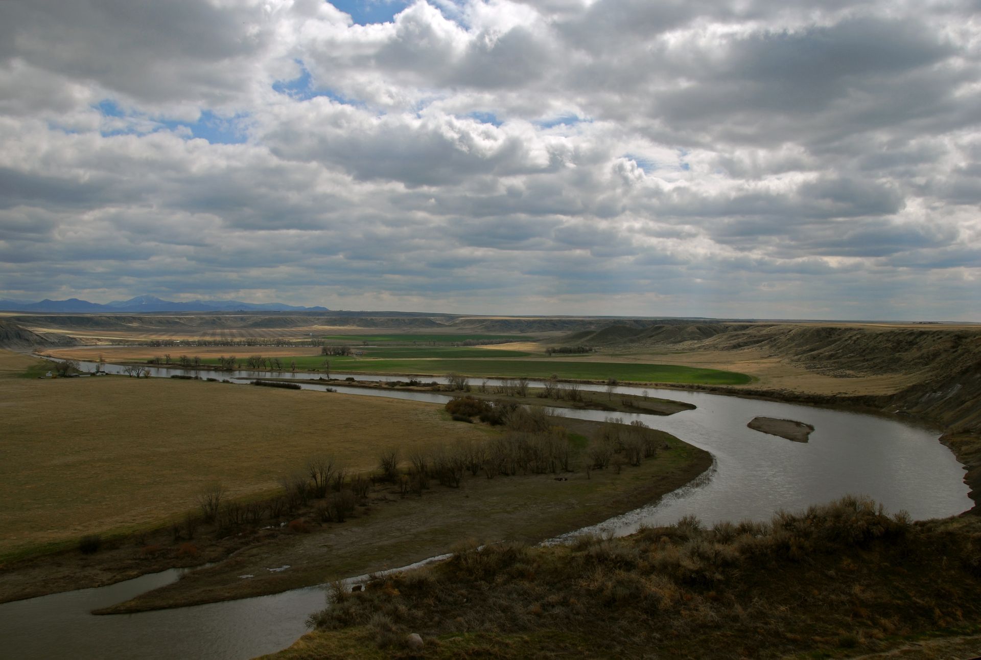 A river flowing through a valley with mountains in the background and clouds in the sky.