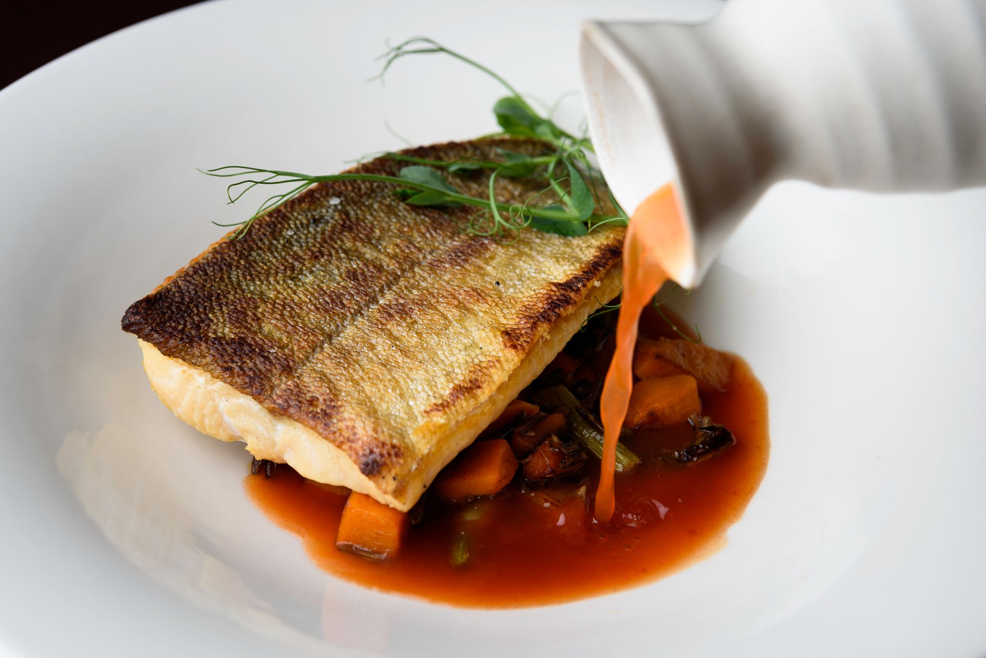 A white plate topped with a piece of fish and sauce